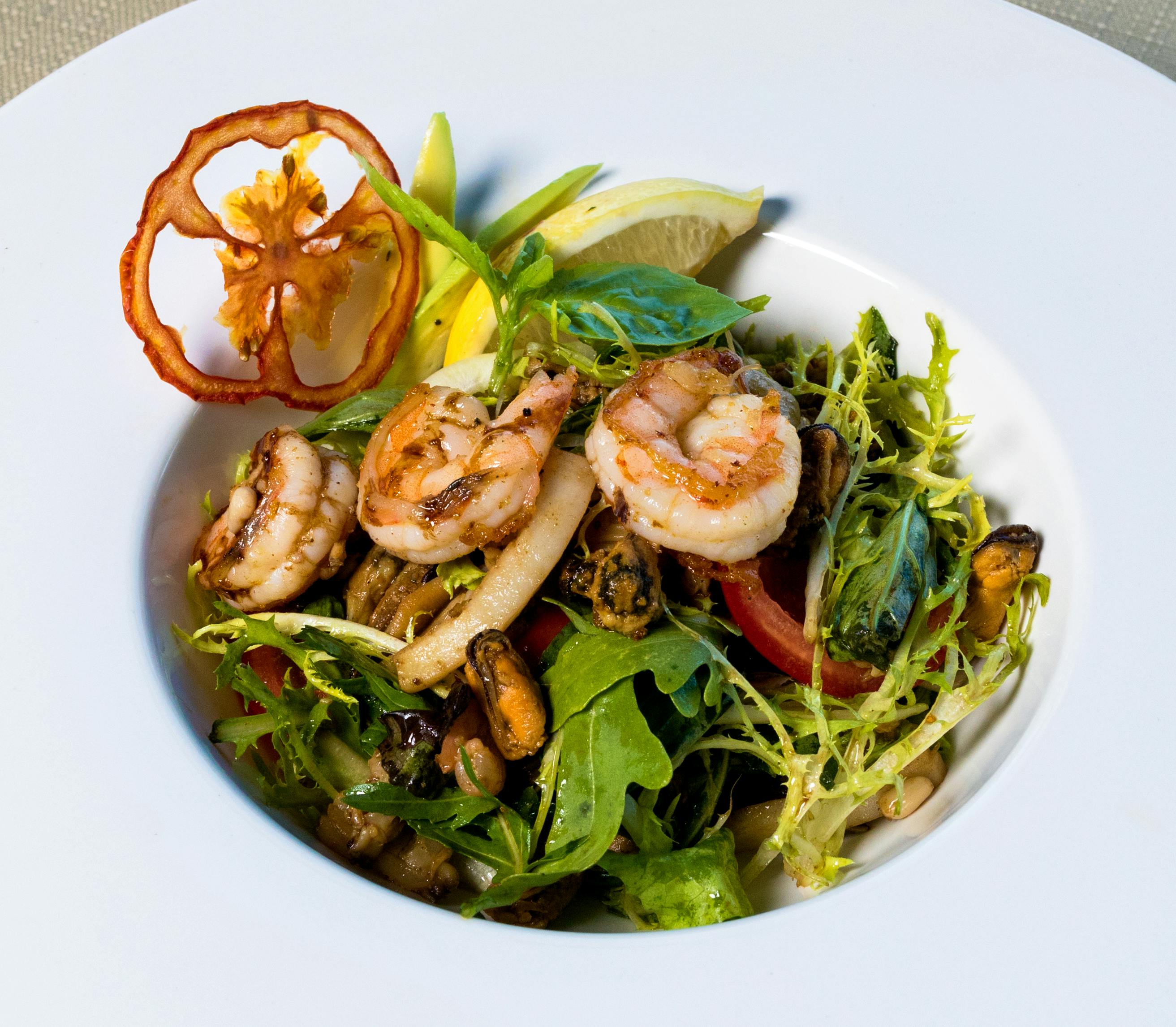 A delicious seafood salad with grilled shrimp, fresh greens, and lemon slice.