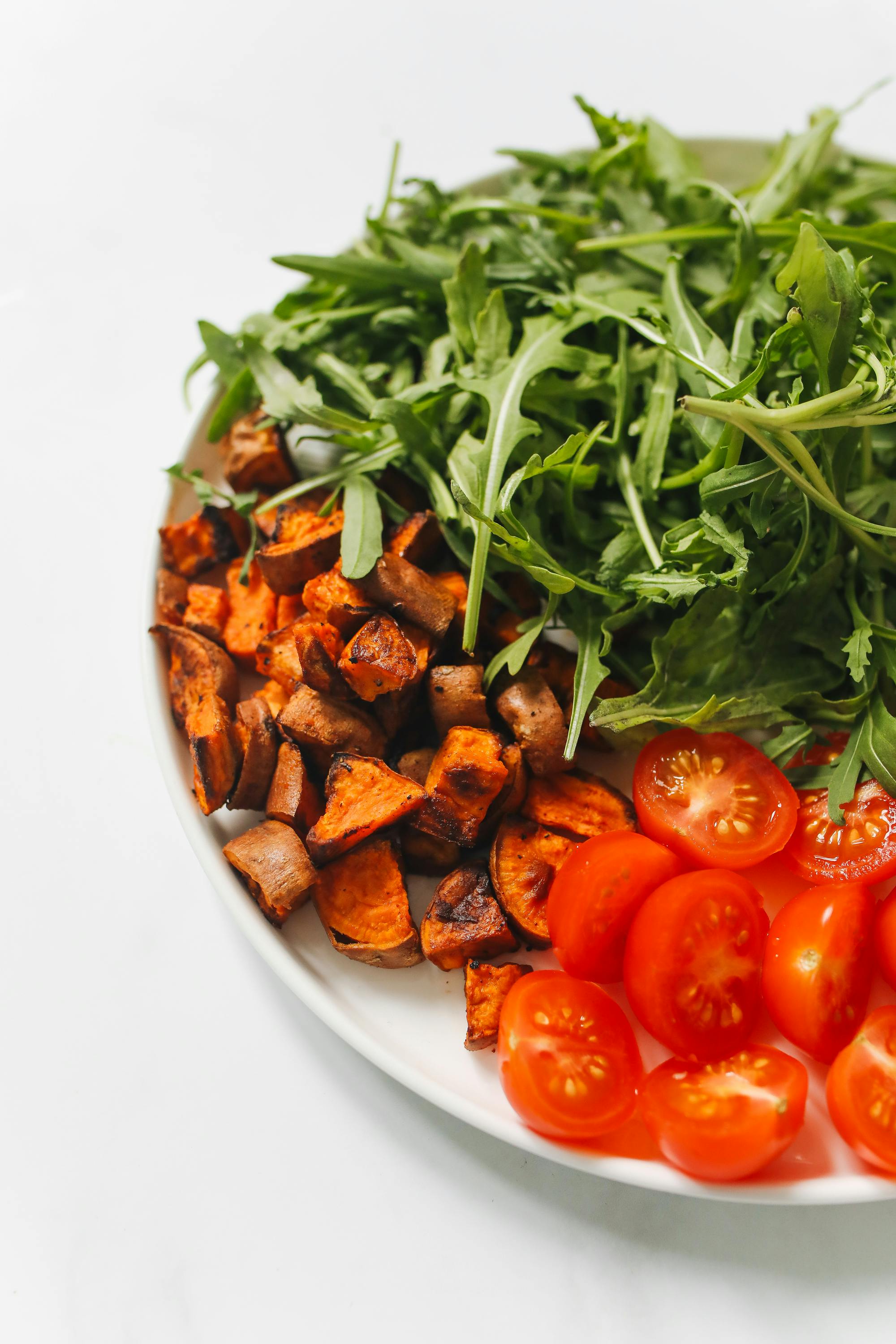 Colorful salad bowl featuring arugula, roasted sweet potatoes, and cherry tomatoes.