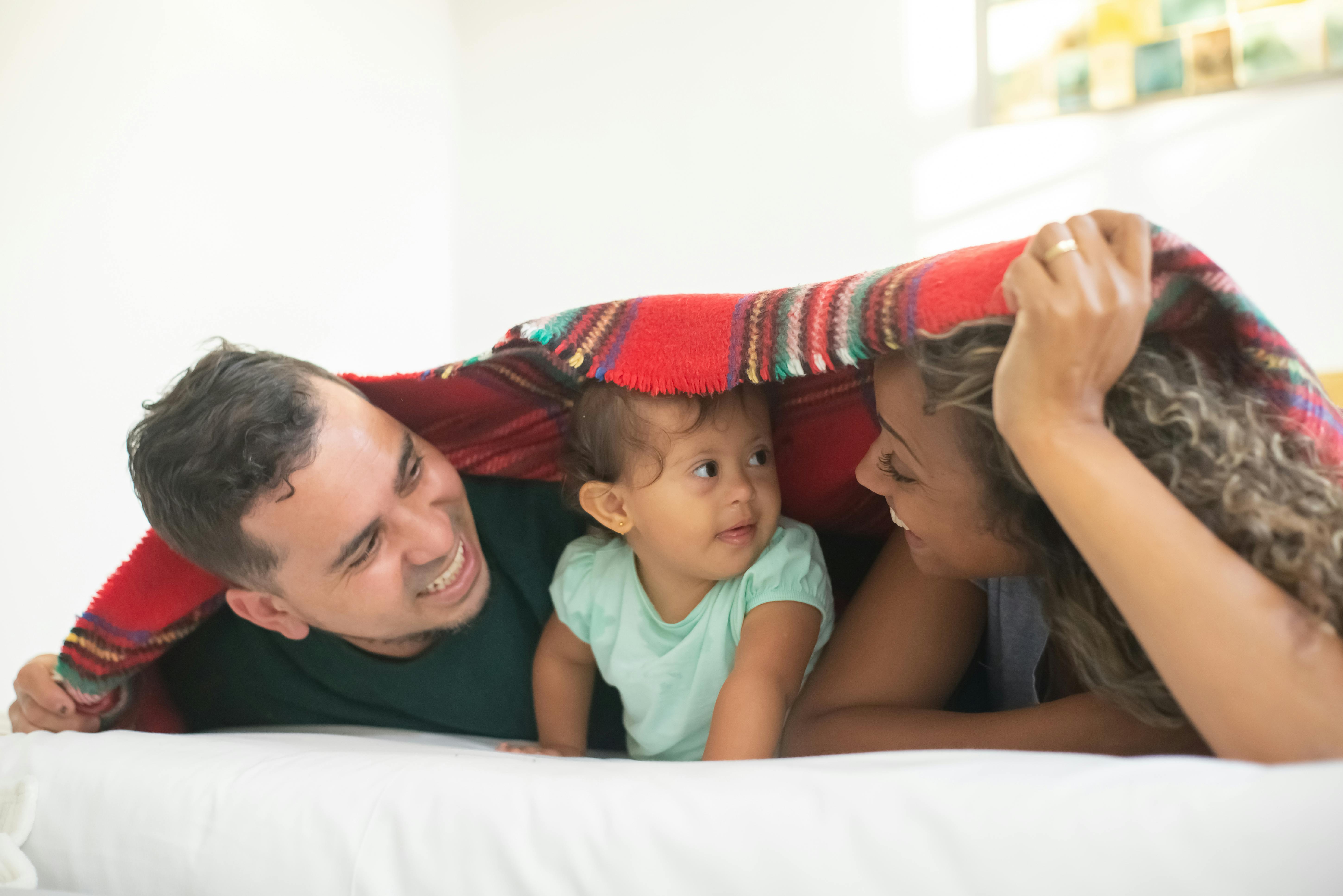 Joyful family of three sharing loving moments under a blanket indoors.